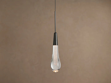Soltaire Pendant, hanging vertically, with a dark nickel cap and a clear, bubble-filled teardrop glass shade glowing warmly.