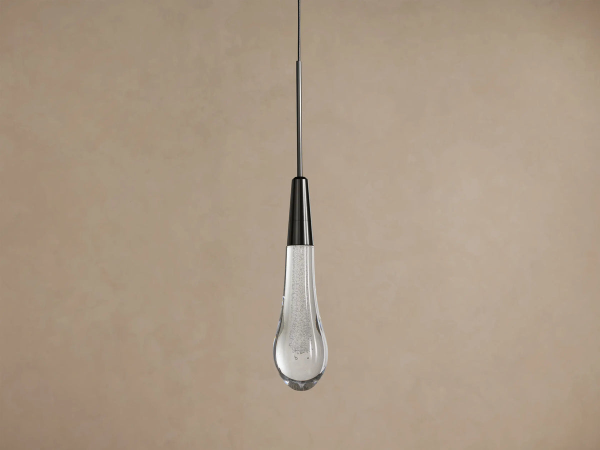 Soltaire Pendant, hanging vertically, with a dark nickel cap and a clear, bubble-filled teardrop glass shade glowing warmly.