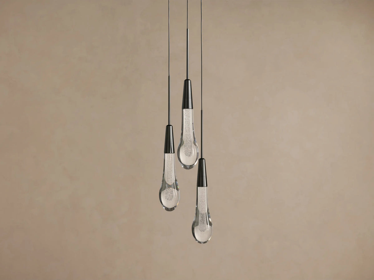 Soltaire Cluster Pendant: Three teardrop-shaped lights with dark metal tops and clear, textured glass bottoms hang from wires.