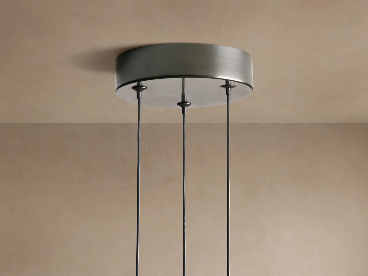 Three Soltaire Cluster Pendants with dark metal tops & teardrop clear glass shades, filled with bubbles & emitting warm light.