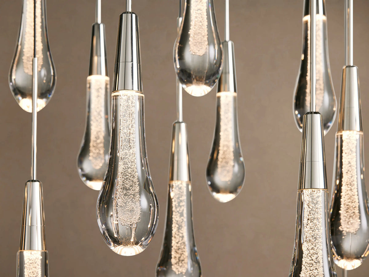 Soltaire Linear Chandelier: Many clear, textured teardrop glass pendants with silver caps hanging on black wires against beige.