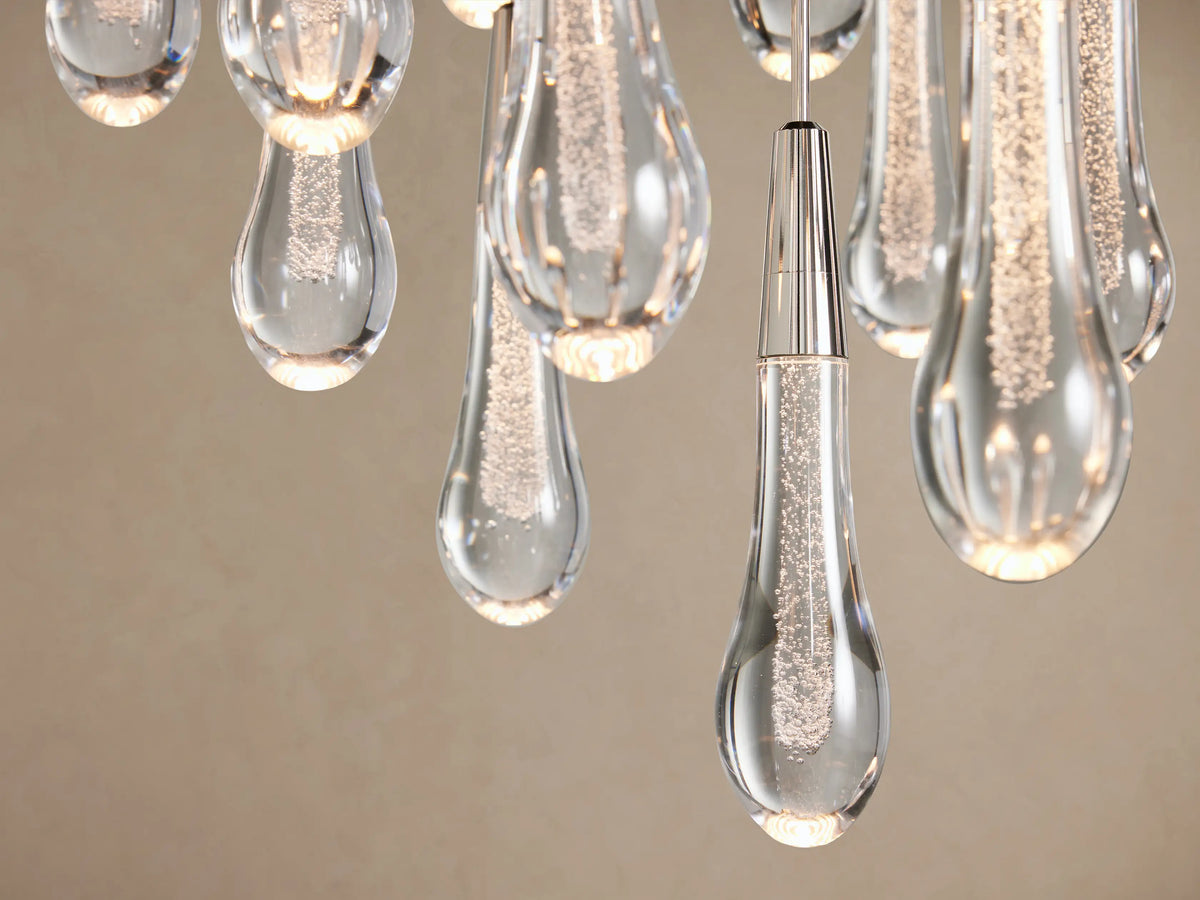 Soltaire Round Chandelier: multiple clear glass teardrop pendants with bubbly texture, silver caps, hanging on beige wall.