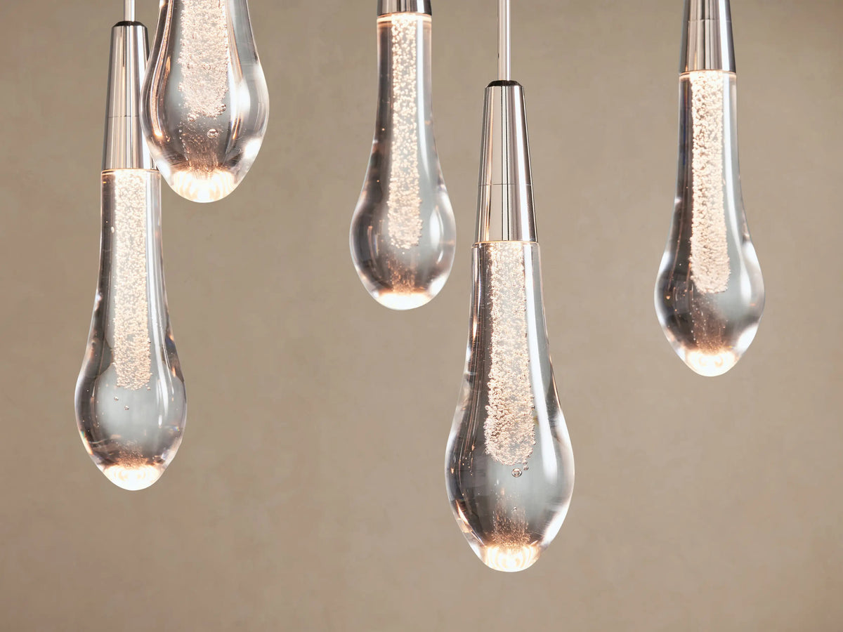 Soltaire Linear Chandelier: multiple teardrop clear glass lights with internal bubbles & silver caps, hanging at varying lengths.
