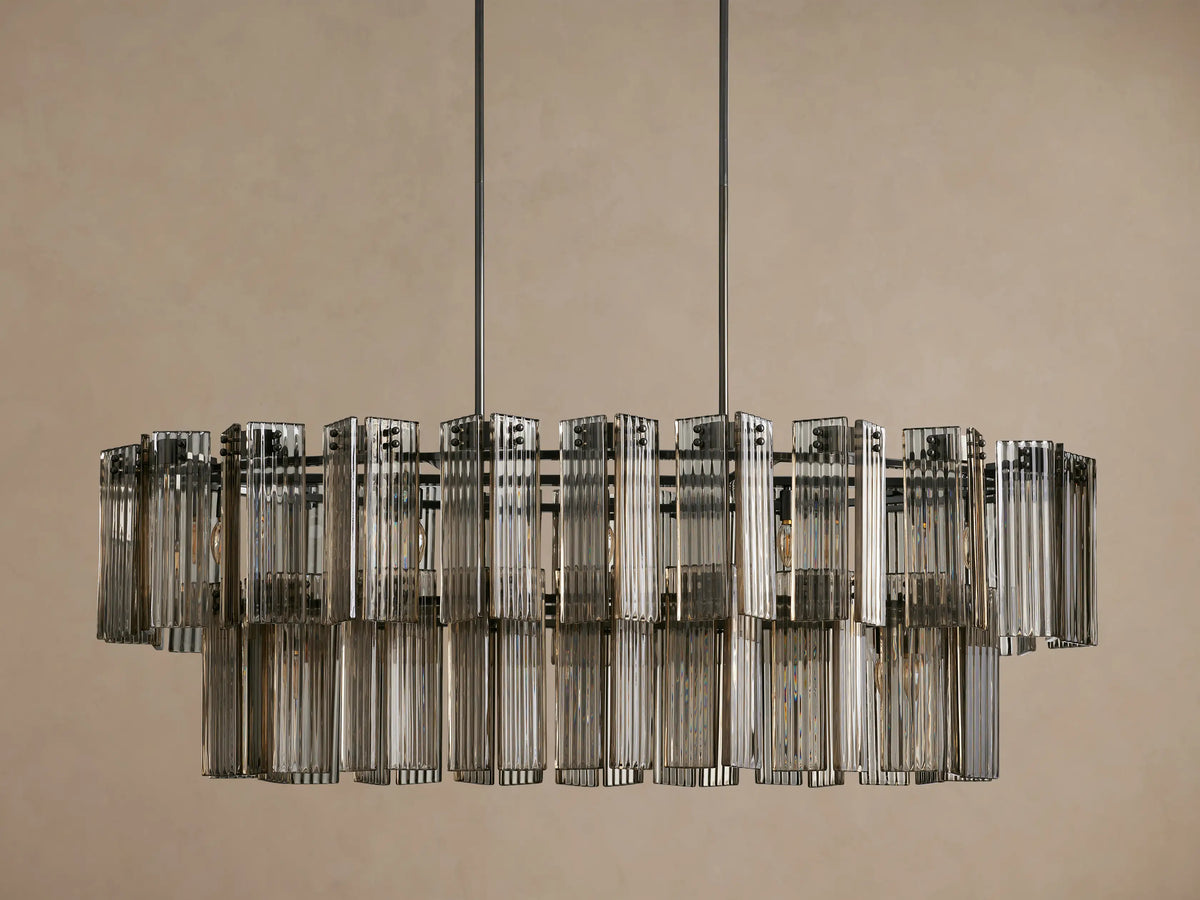 Delsie Oval Tiered Chandelier: Dark burnished metal frame supporting two tiers of illuminated clear fluted glass rods, hanging centrally.