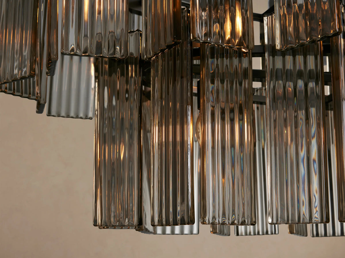 Delsie Oval Tiered Chandelier, dark metal frame with two tiers of clear ribbed glass rods, against a beige background.