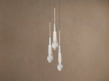 Three Soltaire Cluster Pendants with clear tear-drop glass shades, silver caps, and glowing textured interiors hanging against a brown wall.