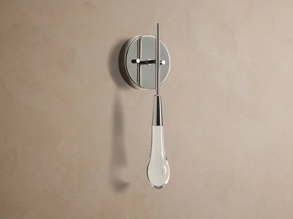 Soltaire Sconce with a shiny nickel backplate, featuring a glowing, clear tear-drop glass light fixture with internal bubbles.