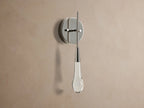 Soltaire Sconce with a shiny nickel backplate, featuring a glowing, clear tear-drop glass light fixture with internal bubbles.