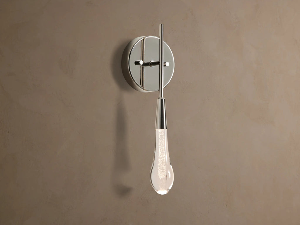 Soltaire Sconce with a shiny nickel backplate, featuring a glowing, clear tear-drop glass light fixture with internal bubbles.