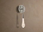 Soltaire Sconce with a shiny nickel backplate, featuring a glowing, clear tear-drop glass light fixture with internal bubbles.