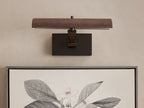 Abel Picture Light Sconce, a dark bronze curved light bar with warm LED light, mounted on a wall above a framed botanical artwork.