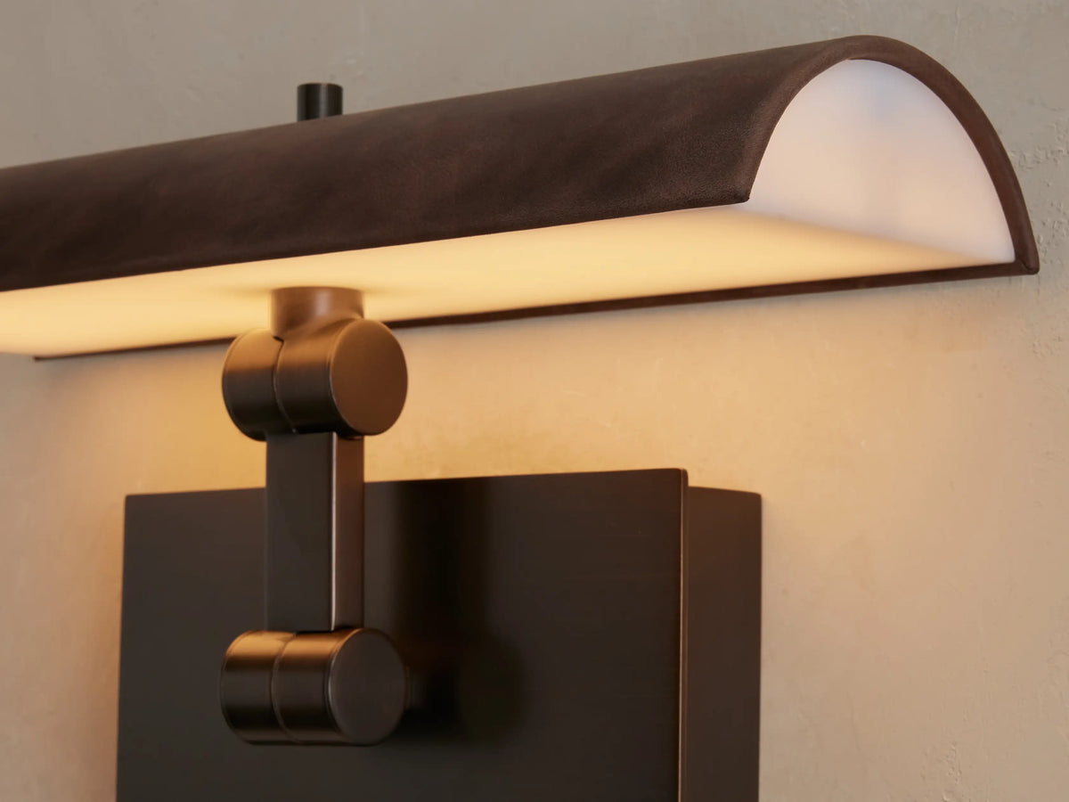 Abel Picture Light Sconce: dark brown leather-wrapped steel light and bronze backplate, mounted on a neutral wall above framed art.
