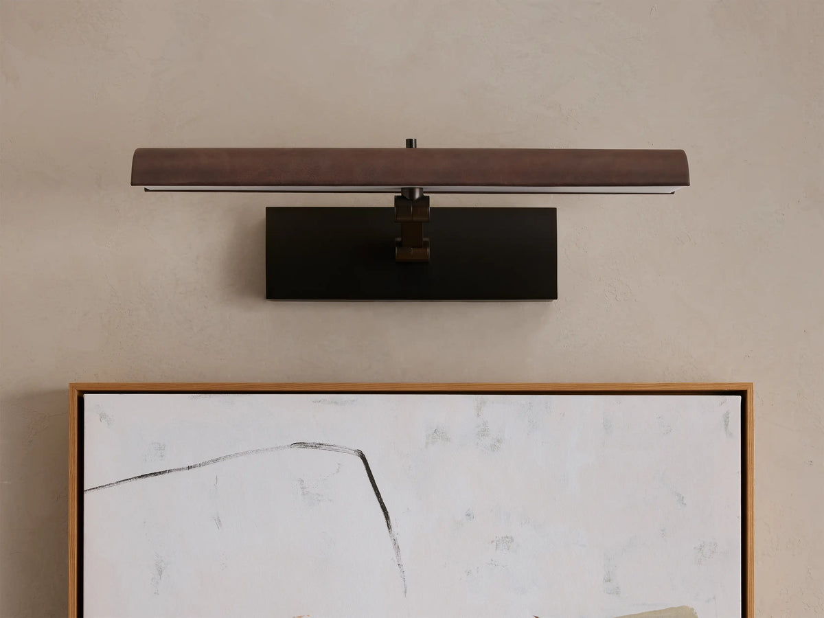 Abel Picture Light Sconce, dark brushed bronze, horizontally mounted over an abstract artwork, casting warm LED light.