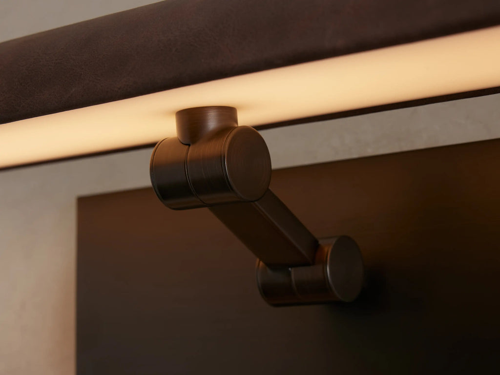 Abel Picture Light Sconce: horizontal brown leather-wrapped light, black backplate, mounted on a wall over abstract art.