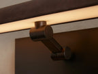 Abel Picture Light Sconce: horizontal brown leather-wrapped light, black backplate, mounted on a wall over abstract art.