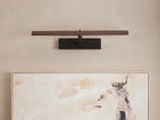 Abel Picture Light Sconce with a dark bronze finish, mounted horizontally on a light wall, casting a warm glow onto an abstract painting.