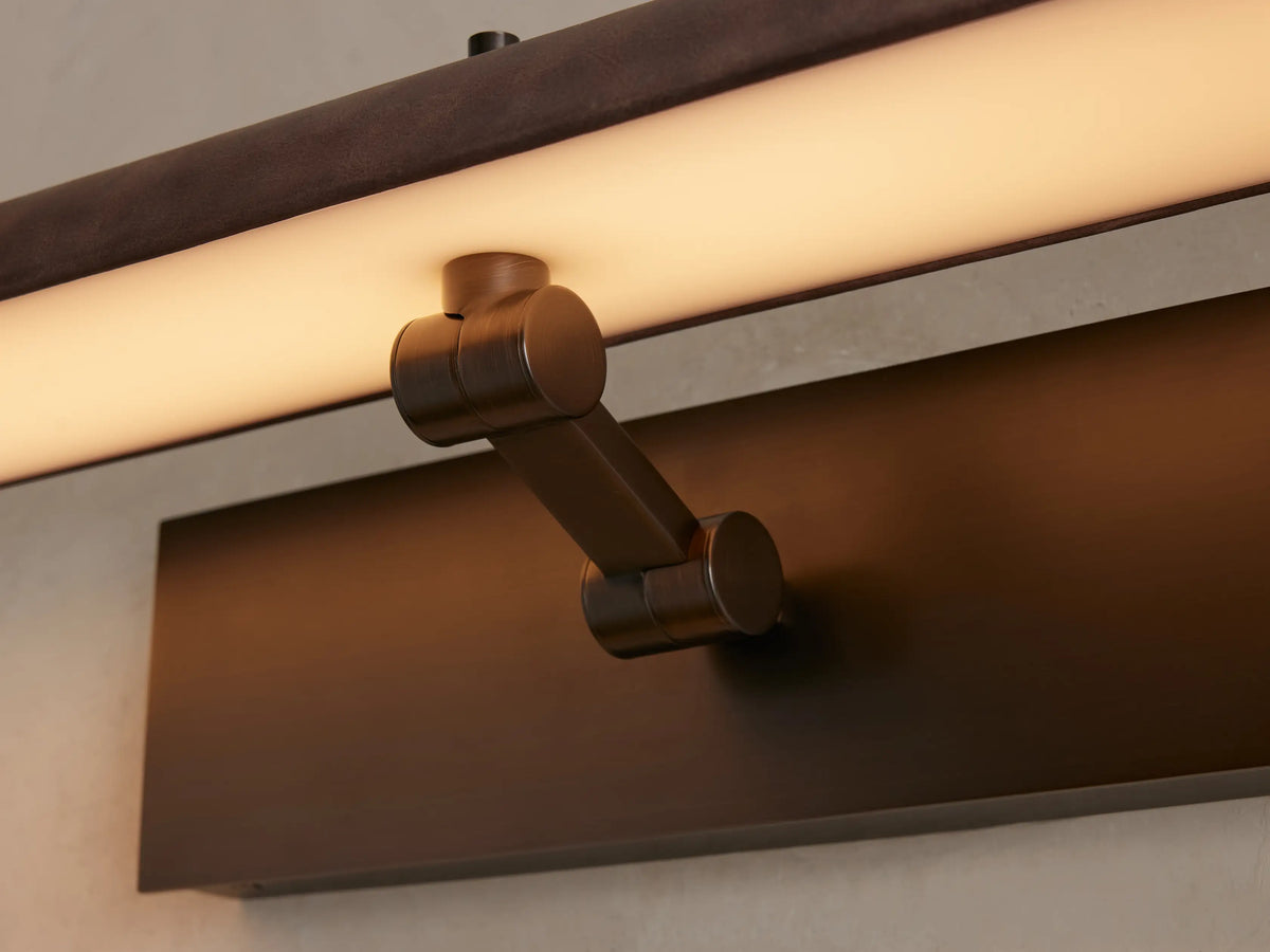 Abel Picture Light Sconce, brown leather-wrapped bar on brushed bronze backplate, illuminating an abstract painting.