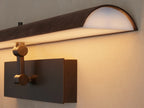 Horizontal Abel Picture Light Sconce with dark leather-wrapped bar emitting warm LED light, mounted on a brushed bronze backplate.