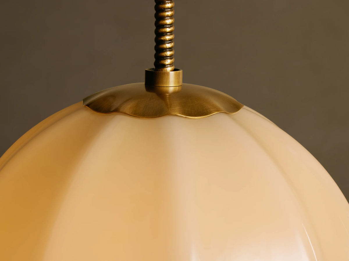 Agnes Pendant featuring a cream paneled globe shade suspended by an antique brass stem against a light beige wall.