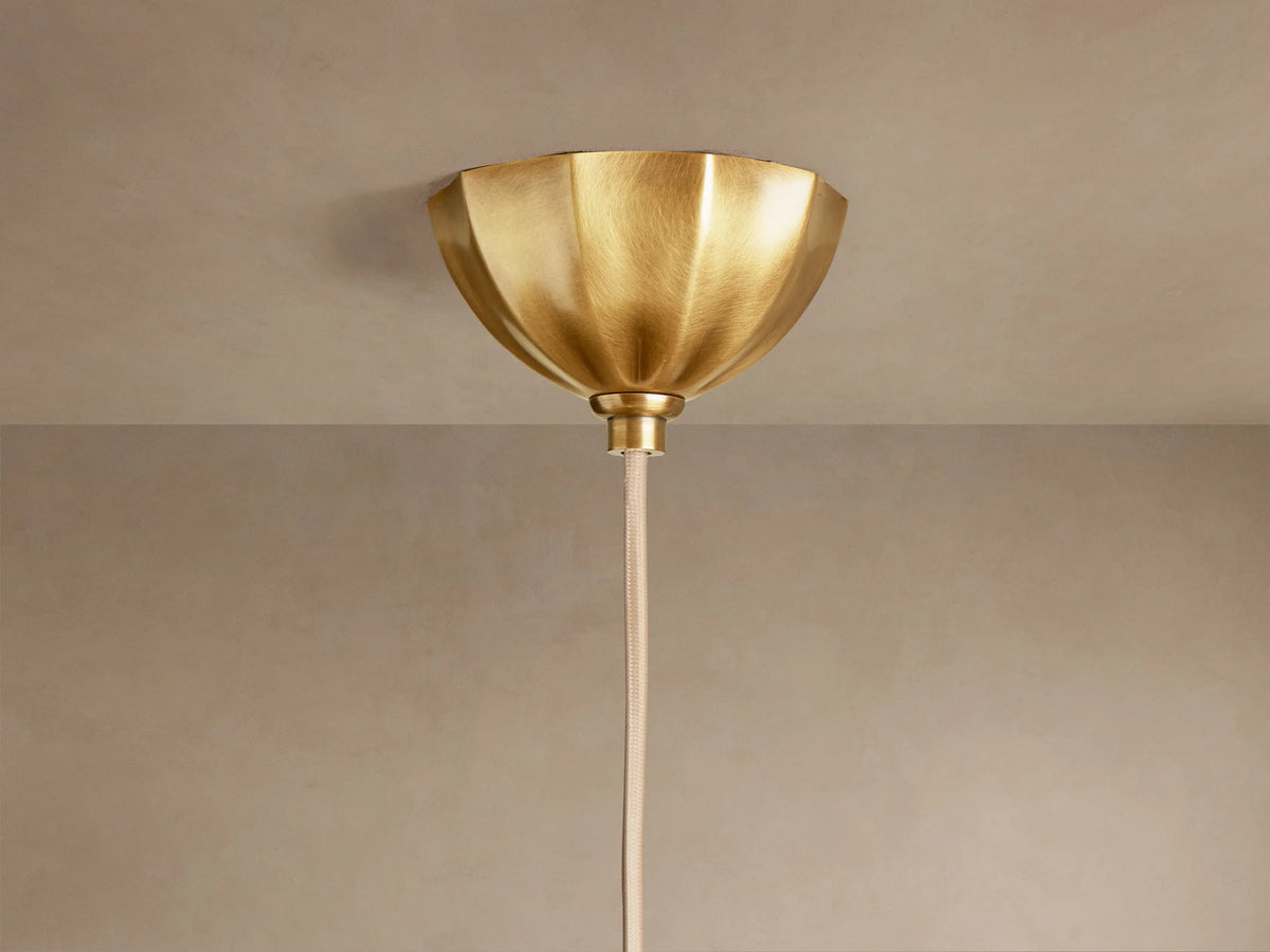Close-up of Agnes Pendant with antique brass ribbed stem, scalloped brass fitting, and large, domed cream paneled glass shade.