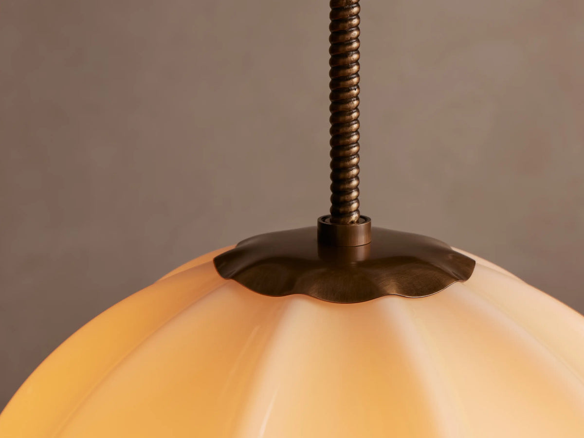 Agnes Pendant light: Spherical, paneled cream glass shade with an antique brass stem, hanging against a light neutral background.