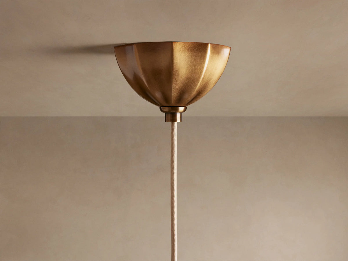 Close-up of Agnes Pendant with illuminated cream paneled glass shade, antique brass scalloped fitting, and spiraled rod.