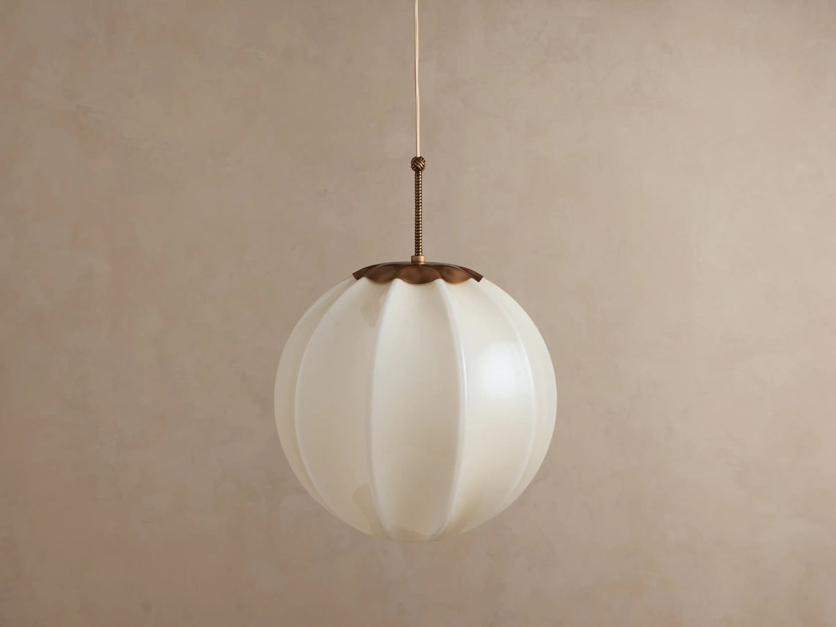 Agnes Pendant: spherical paneled cream glass shade with an antique brass cap, hanging and illuminated with a warm glow.