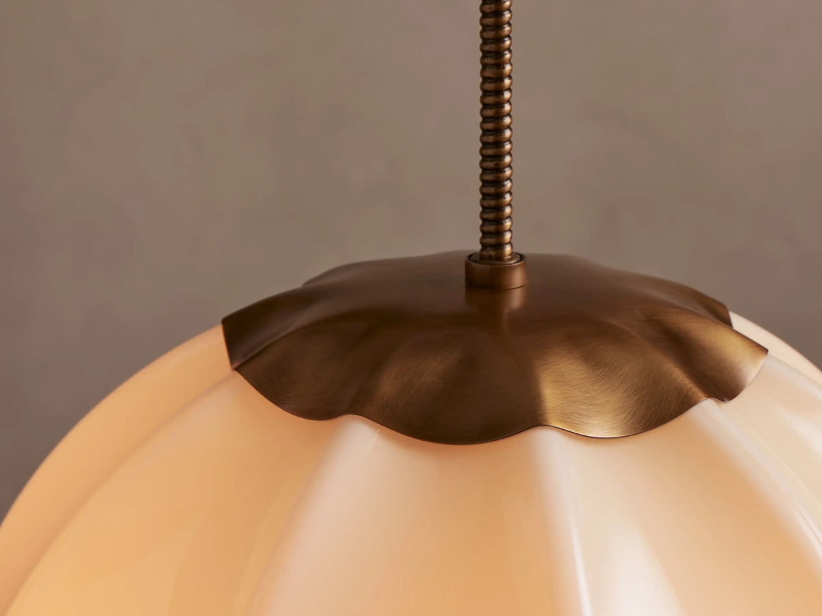 Agnes Pendant: Cream paneled glass globe light with antique brass top accents, hanging against a light beige wall.