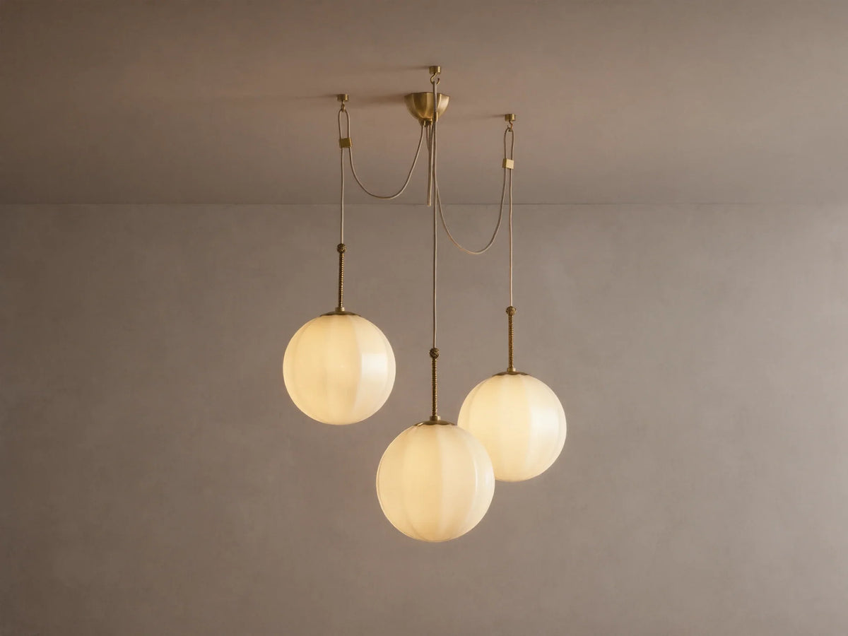 Agnes Chandelier: 3 glowing, paneled cream glass globes suspended from antique brass hardware, draped on a light ceiling.