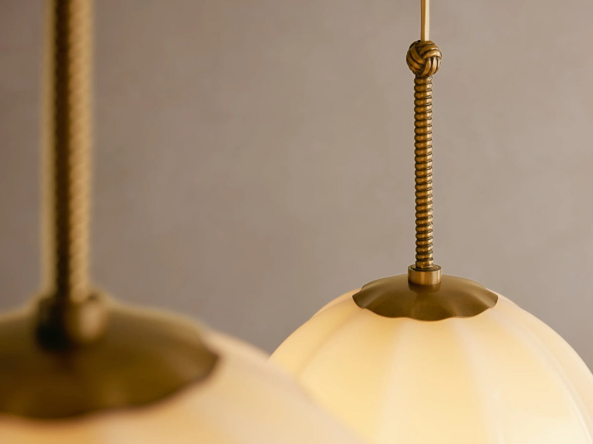 Agnes Chandelier: three cream ribbed glass globes suspended by draped antique brass cables from a ceiling.
