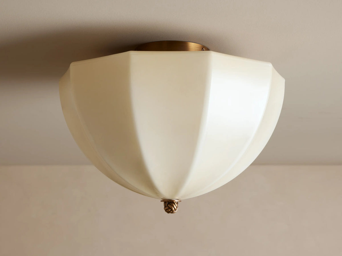 Agnes Flush Mount with paneled cream glass shade & antique brass details, emitting a warm glow from a ceiling mount.