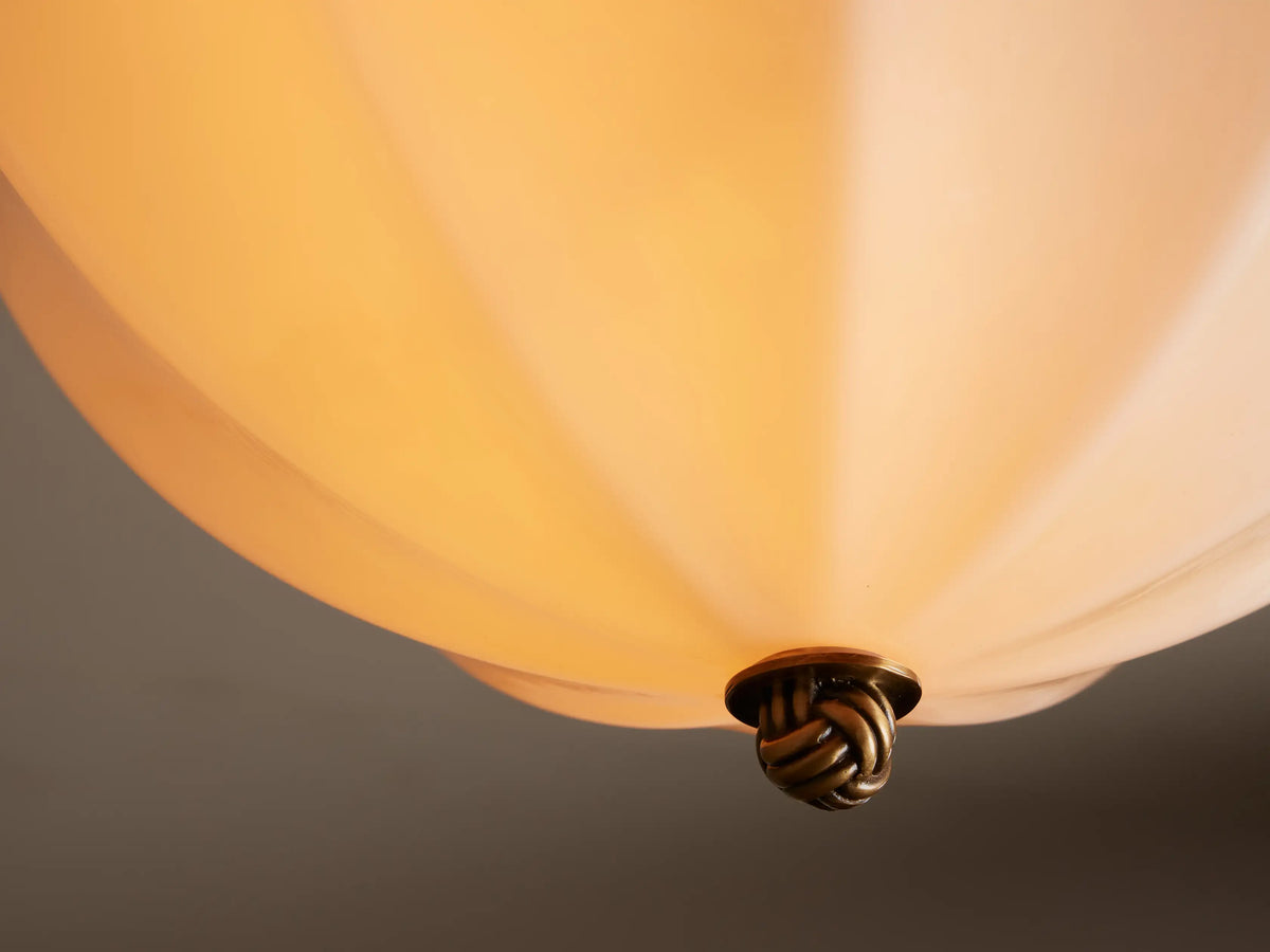 Agnes Flush Mount light fixture with an antique brass base, ornate finial, and cream-colored paneled glass shade.