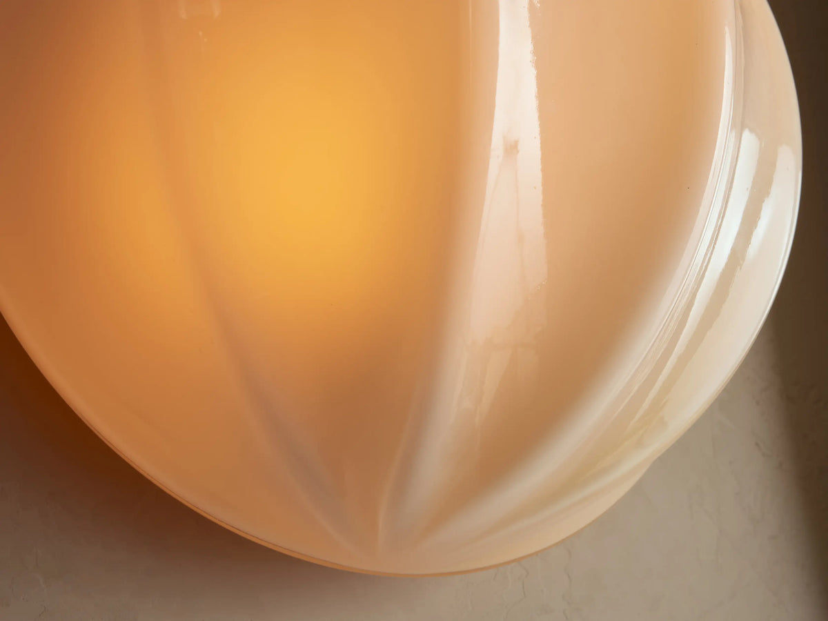 Agnes Clamshell Sconce: Cream ribbed glass wall light, rounded, mounted on a light beige wall, next to a dark brown mirror.
