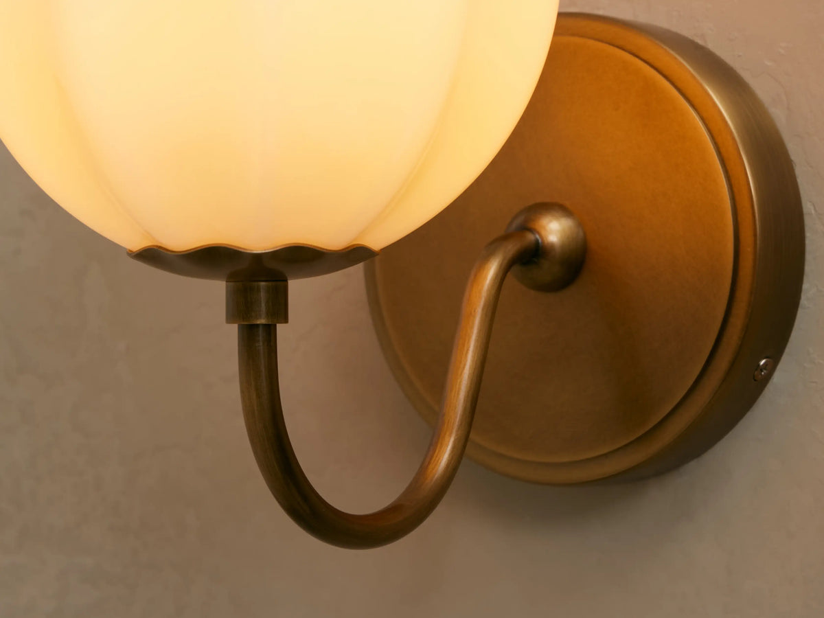 Agnes Gooseneck Sconce with antique brass finish, curved arm, and a paneled cream glass globe shade on a light wall.