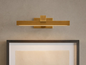 Corinth Picture Light Sconce, brass rectangular bar with LED light, mounted on wall above framed art.