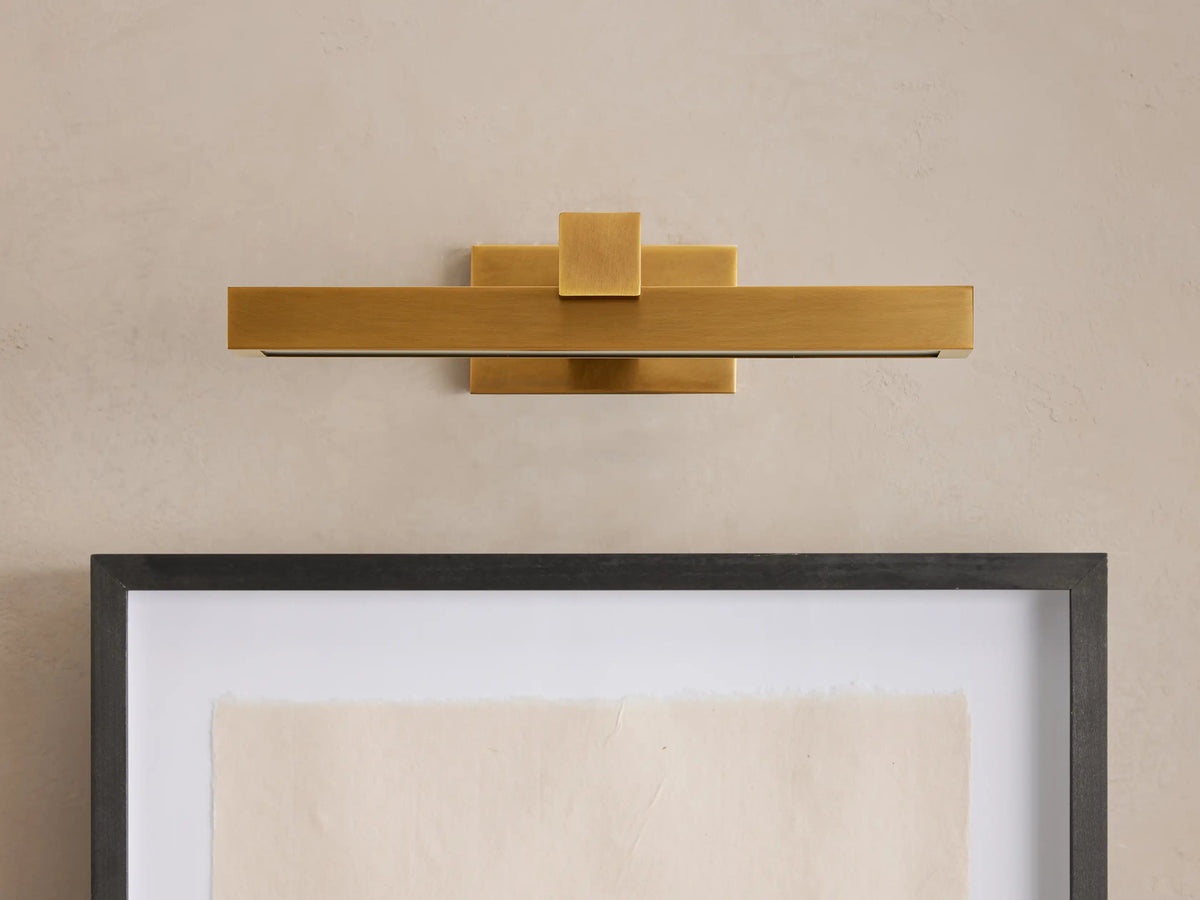 Corinth Picture Light Sconce, brass rectangular bar with LED light, mounted on wall above framed art.