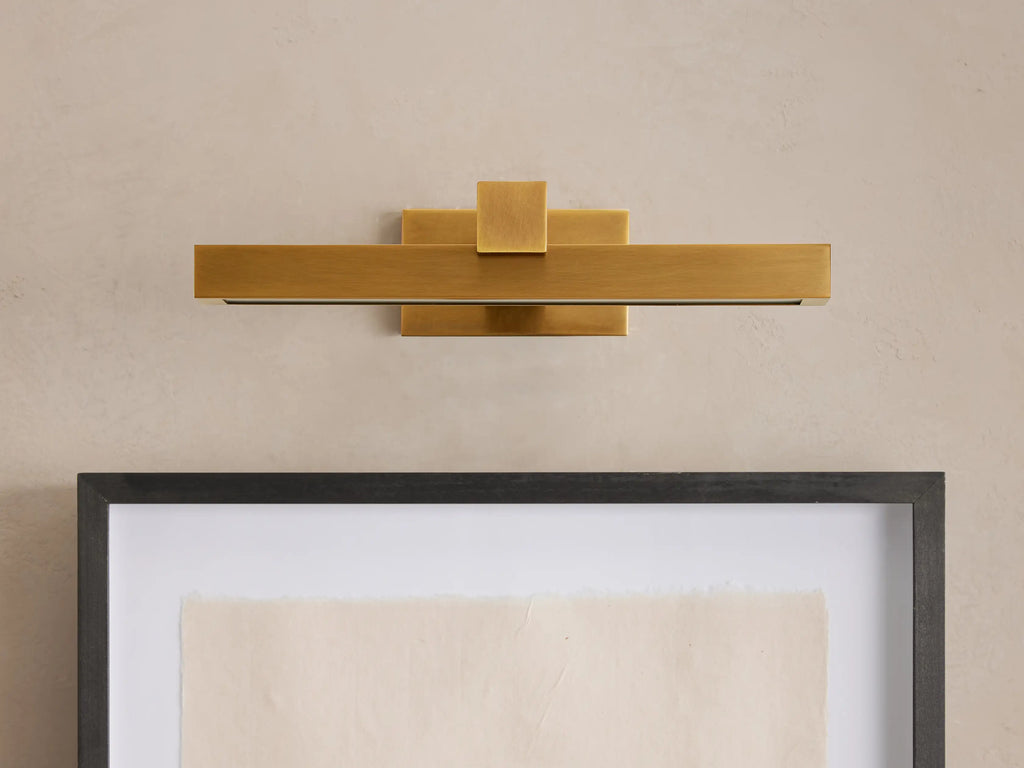 Corinth Picture Light Sconce, brass rectangular bar with LED light, mounted on wall above framed art.