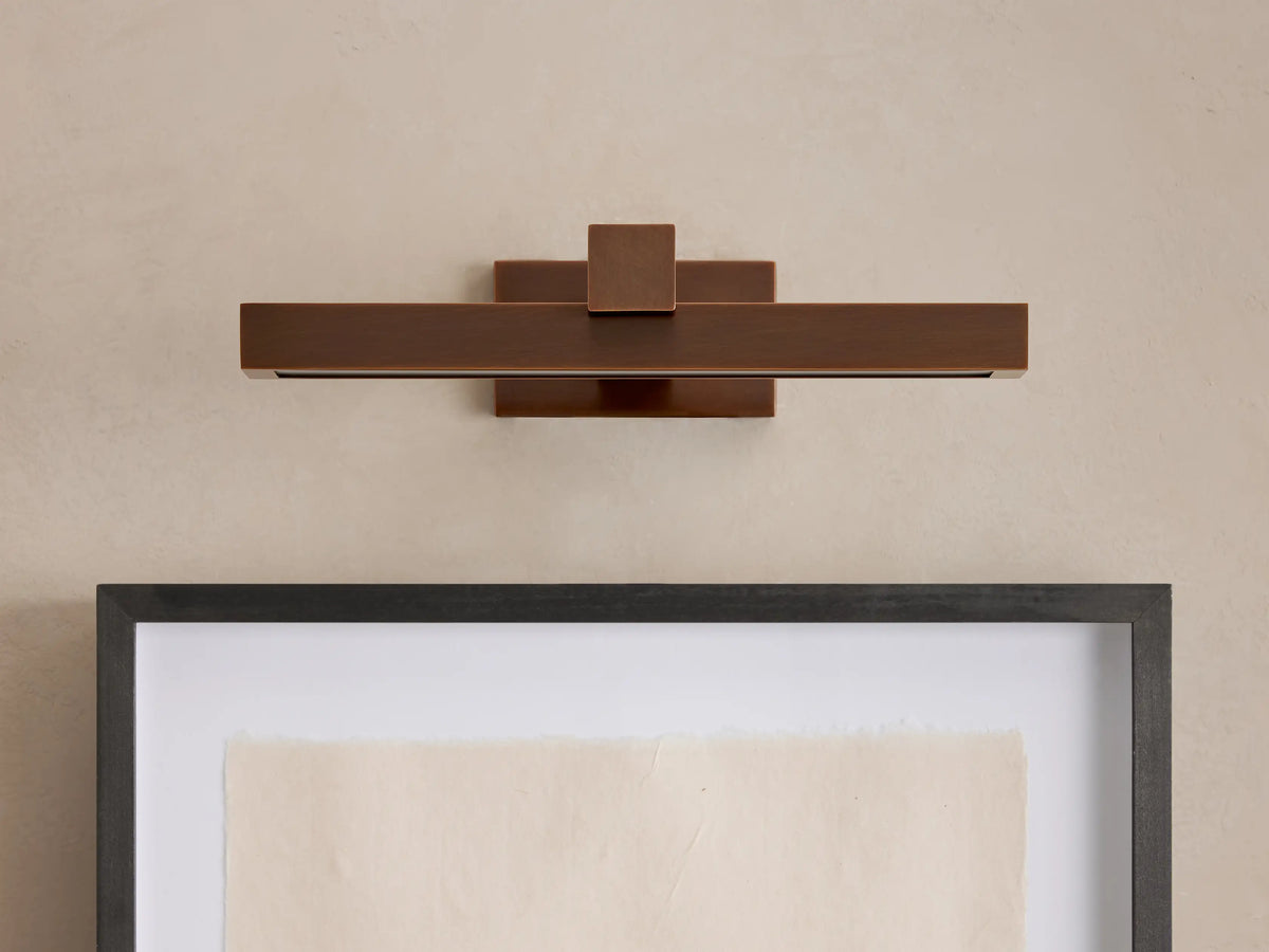 Horizontal Corinth Picture Light Sconce in a dark bronze finish, emitting warm LED light onto a framed artwork below.