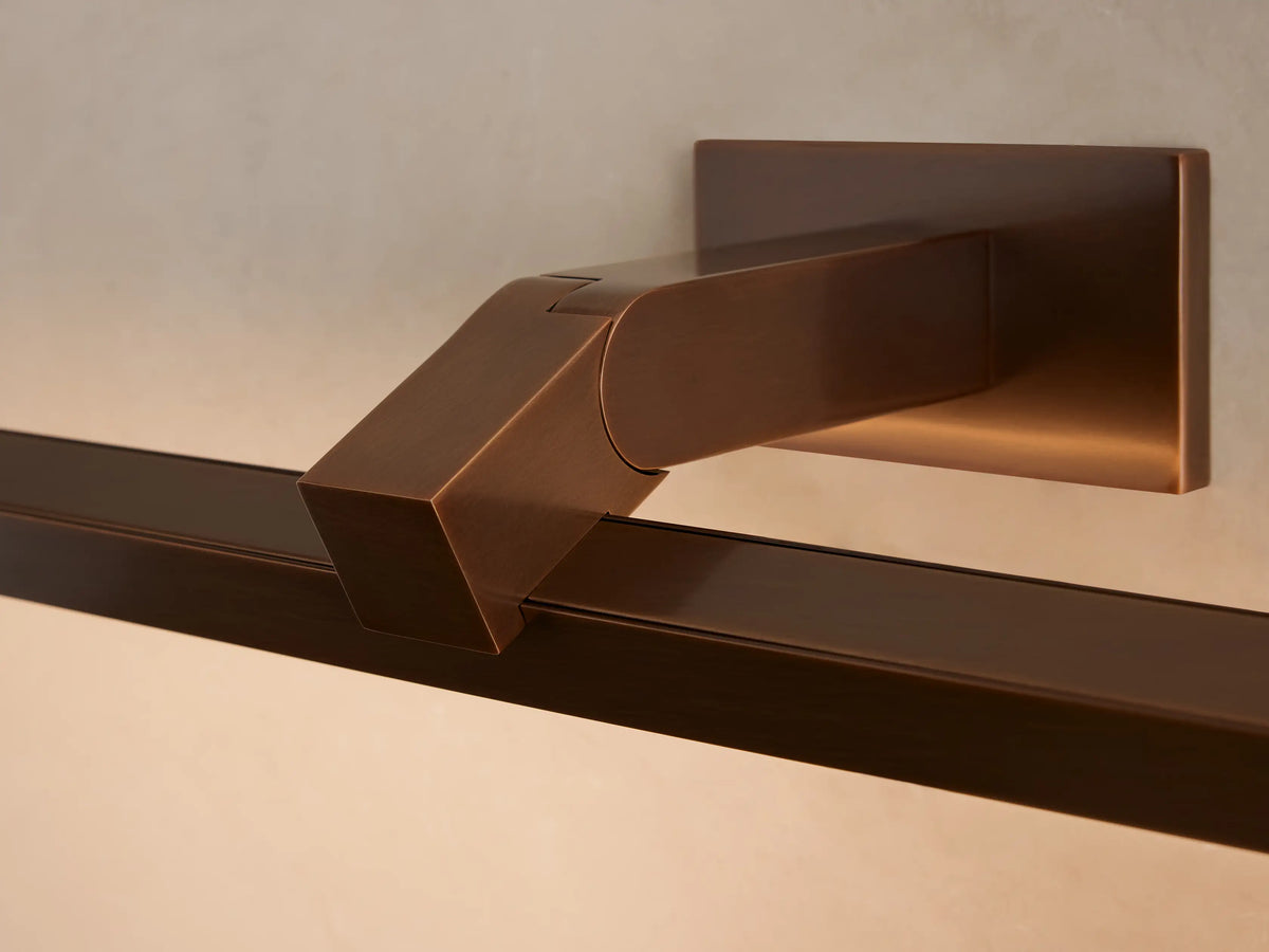 Bronze-finished Corinth Picture Light Sconce with rectangular bar & backplate, mounted on a beige wall above a framed art piece.