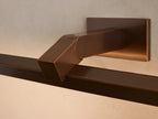 Corinth Picture Light Sconce: a bronze rectangular bar light mounted on a beige wall, positioned above a framed abstract artwork.