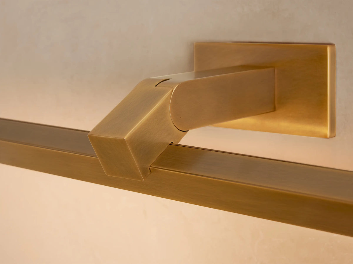 Corinth Picture Light Sconce: Horizontal brass bar light mounted on a beige wall above an abstract painting.