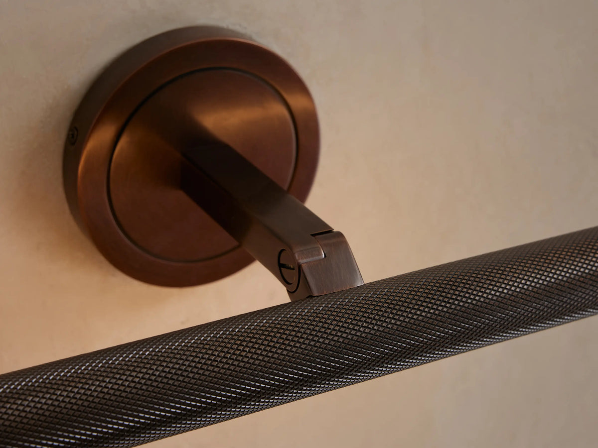 Close-up of a Monroe Picture Light Sconce in antique brass with knurled detailing, mounted on a light wall, light glowing below.