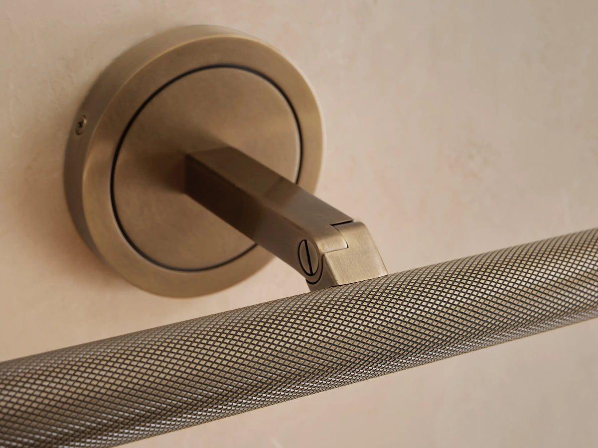 Close-up of an antique brass Monroe Picture Light Sconce on a beige wall, featuring a round base and a knurled light bar.