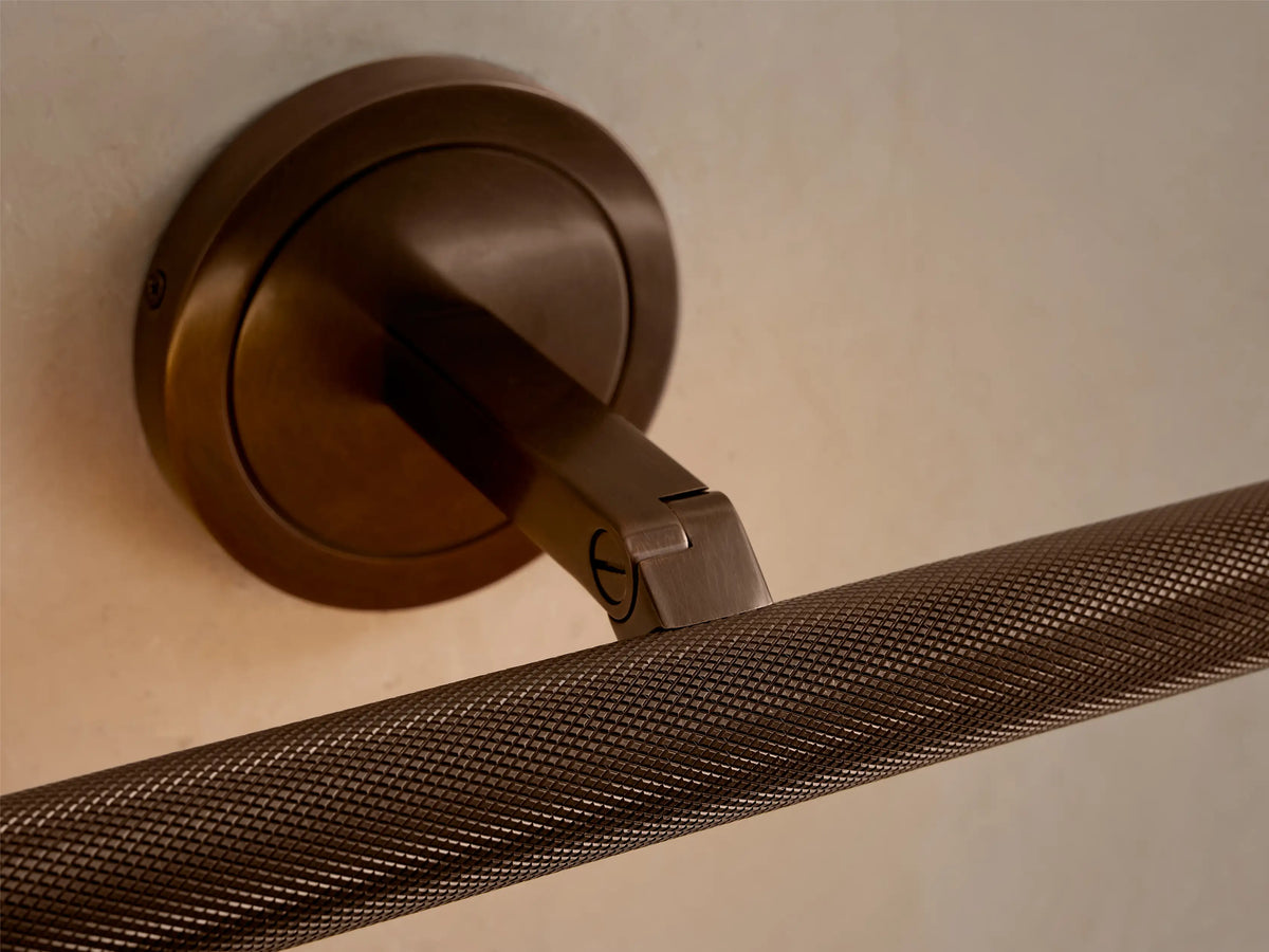 Monroe Picture Light Sconce in antique brass with knurled bar, mounted on a cream wall, emitting a soft glow.