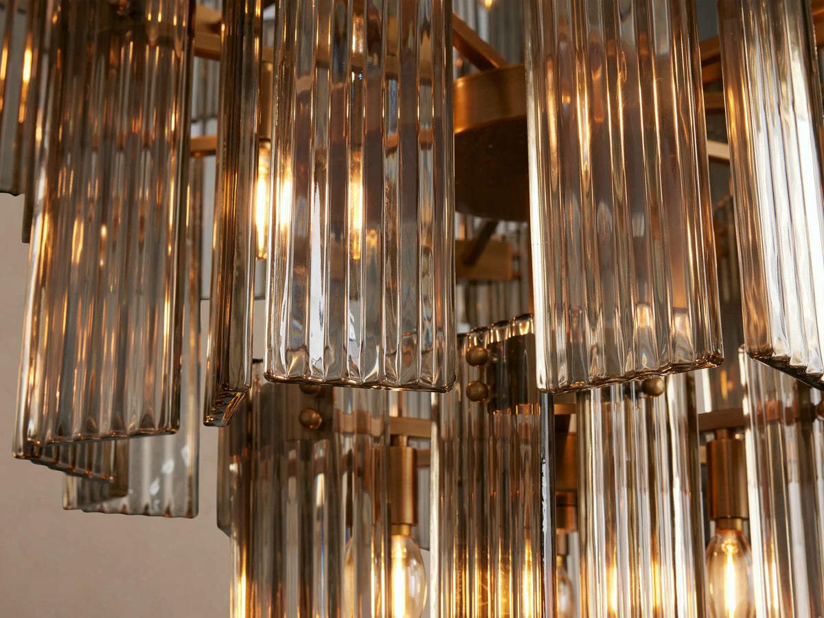Delsie Round Chandelier with multiple tiers of clear fluted glass rods and a brass frame, hanging against a plain wall.