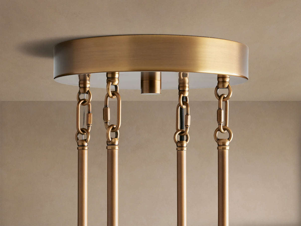 Close-up of Delsie Round Chandelier. Ribbed glass rods hang from a burnished brass frame, glowing with warm light.