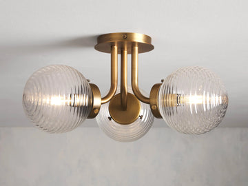 Sayre Flush Mount with burnished brass finish, features three ribbed glass globes attached to a central steel fixture against a light background.