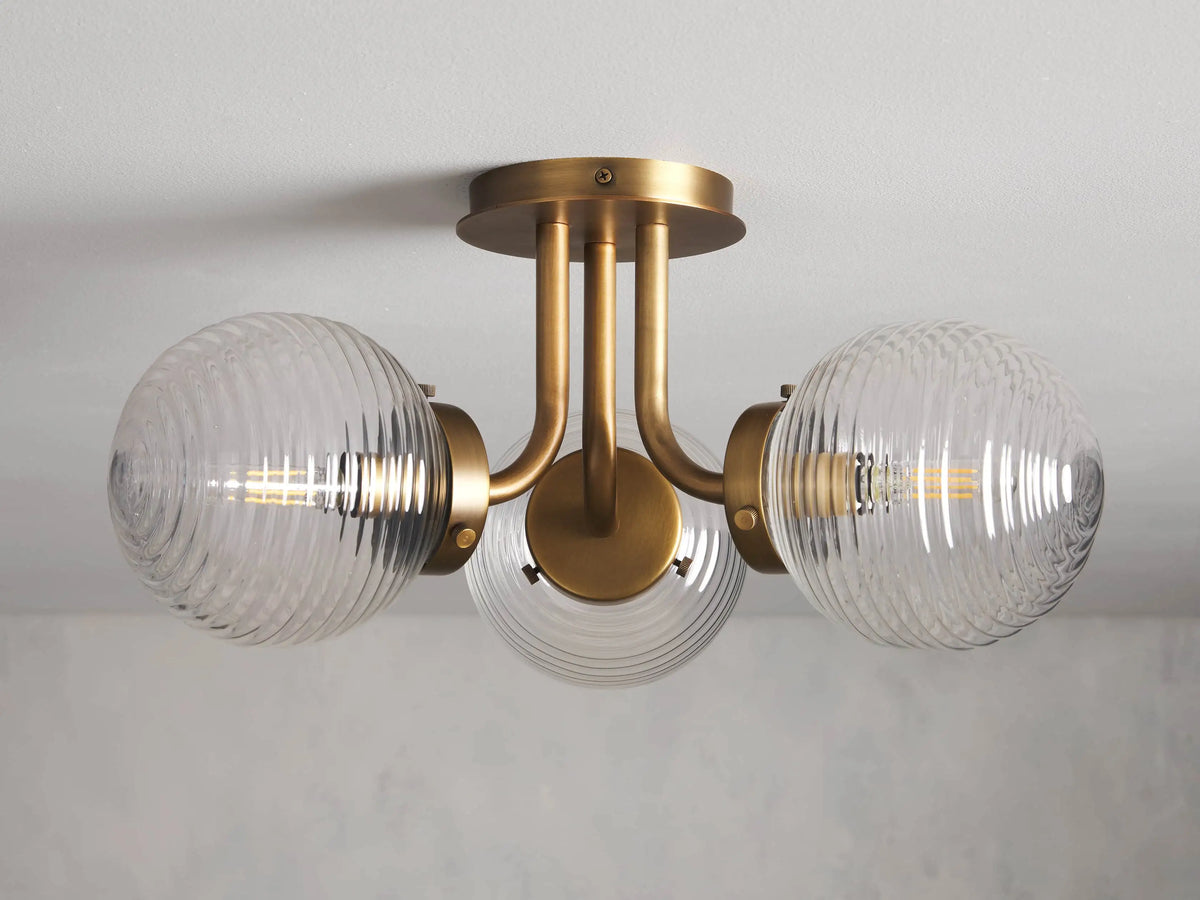 The Sayre Flush Mount features three ribbed glass globes on a burnished brass fixture, mounted flush to a ceiling.