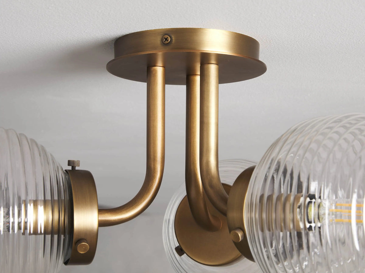Sayre Flush Mount with Burnished Brass finish, two curved arms, ribbed glass globes, attached to a ceiling plate.