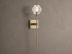 Amoroso Sconce: brass-plated wall light with long rod and illuminated faceted clear crystal shade on a brown wall.